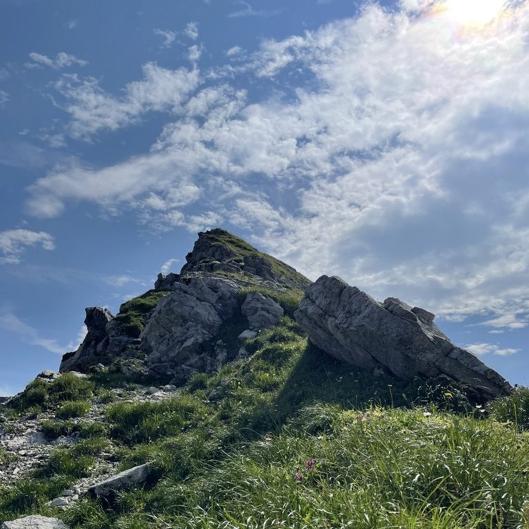 Sonniger Blick hinauf zum Berggipfel mit blauem Himmel und leichten Wolken dahinter